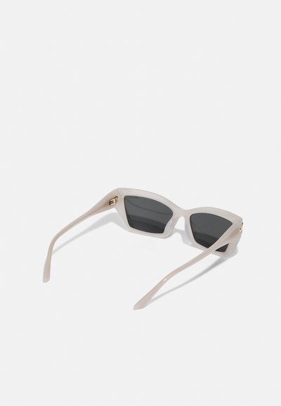 Transparent beige sunglasses with a geometric cat-eye shape, dark lenses, and slender arms featuring gold-toned hardware accents.
