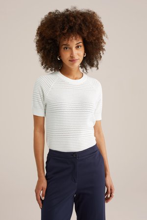 Top bianco a maniche corte lavorato a maglia con un motivo testurizzato di righe e fori, abbinato a pantaloni blu navy con tasche laterali.