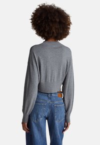 Szary krótki sweter z wyraźnie prążkowanym kołnierzem, luźnymi ramionami i długimi rękawami, zestawiony z niebieskimi, wysokim stanem jeansami z kieszeniami.