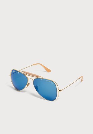 Γυαλιά ηλίου σε στυλ aviator με χρυσό μεταλλικό σκελετό, μπλε καθρέφτη φακούς και μπεζ άκρα στα βραχίονες σε ανοιχτό φόντο.