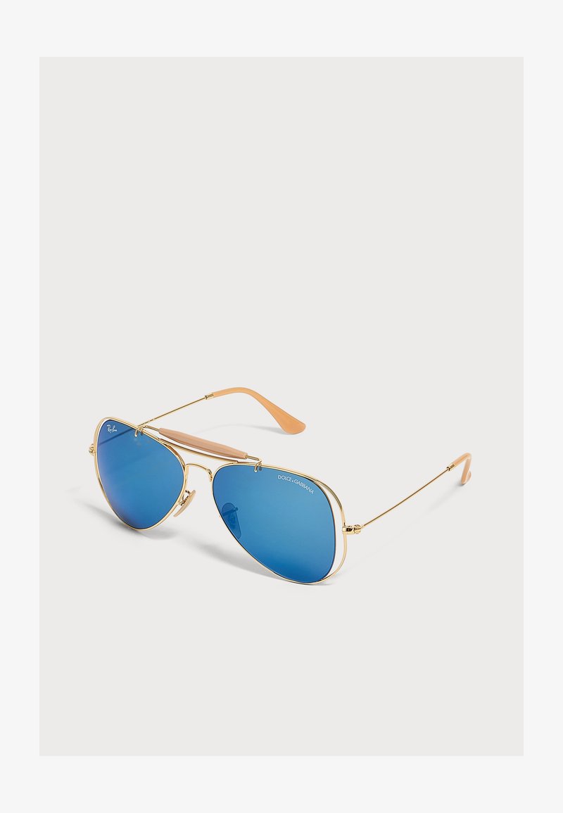Γυαλιά ηλίου σε στυλ aviator με χρυσό μεταλλικό σκελετό, μπλε καθρέφτη φακούς και μπεζ άκρα στα βραχίονες σε ανοιχτό φόντο.