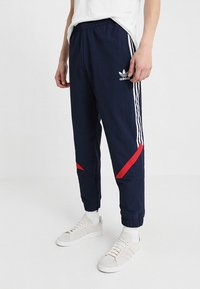 Pantalones deportivos de color marino con rayas blancas y acentos rojos, cintura elástica, puños ajustados y logo en contraste en el muslo superior.