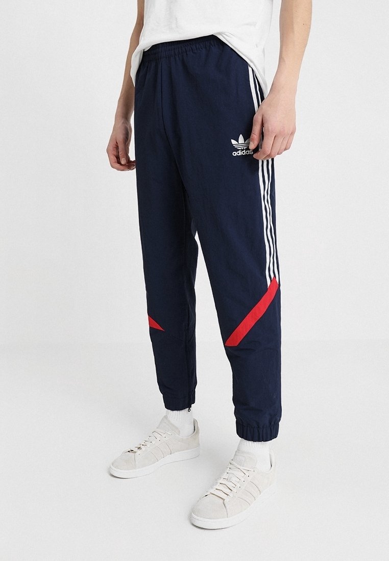 Pantaloni sportivi navy con strisce bianche e dettagli rossi, vita elastica, polsini affusolati e logo a contrasto sulla coscia superiore.