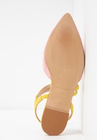 Semelle d'une sandale rose à bout pointu avec des brides jaunes, taille 37, fabriquée en Espagne, posée contre une surface blanche.