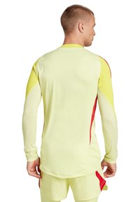 Langsleeve sporttop in felgeel met rode accenten aan de zijkanten, gemaakt van een gladde, rekbare stof met een aangesloten ontwerp.