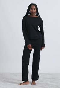 Črno majico z dolgimi rokavi in širokim izrezom okrog vratu, v kombinaciji z ujemajočimi hlačami. Obe sta izdelani iz mehke tkanine z rahlo sproščenim krojem in subtilnimi detajli na robovih.