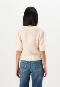Strickpullover mit kurzen Ärmeln, in Cremefarbe mit rosa Streifen, strukturiertem Muster und geripptem Saum. Kombiniert mit blauen High-Waist-Jeans.
