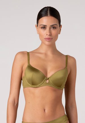 Donna con capelli scuri raccolti indossa un reggiseno in raso verde oliva con sottili spalline e un piccolo dettaglio a occhiello al centro.