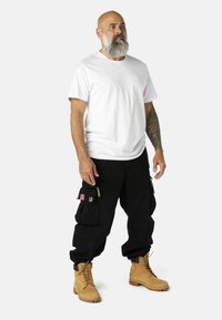Juodi kargo kelnės su daugybe kišenių, baltas marškinėlių apykaklės T-shirt ir rudos darbo botas. Apranga pasižymi praktišku dizainu ir patvariomis medžiagomis.