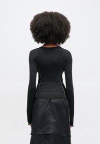 Čierne tričko s dlhým rukávom, priliehavého strihu, s bielym kontrastným prešívaním pozdĺž švov a okrúhlym výstrihom.