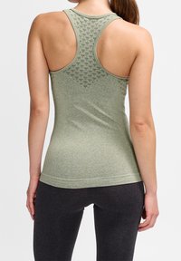 Zelené atletické tílko s texturovaným vzorem na zádech, střihem racerback a přiléhavým tvarem. Tkanina vypadá měkce a pružně, v kombinaci s tmavými legínami.