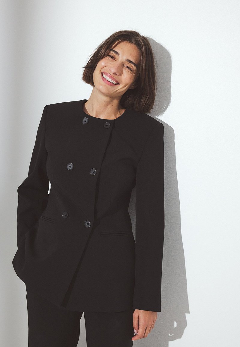 Svart dubbelknäppt kavaj med långa ärmar, med sex runda knappar, skräddarsydd passform och lätt axelpadding. Slät textur.