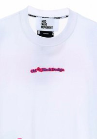 Camiseta blanca de manga corta con cuello redondo, que presenta "Old Black Design" bordado en rojo y azul en la parte delantera. Etiqueta de la marca en el interior del cuello.