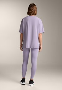 T-shirt oversized viola con maniche corte, abbinato a leggings viola e scarpe da ginnastica nere. Tessuto morbido con una vestibilità comoda.