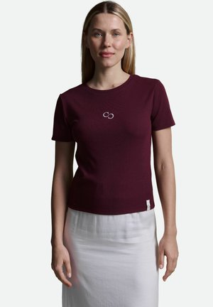 Burgunderfarbendes kurzärmliges geripptes T-Shirt mit glatter Textur und silbernem Logoakzent auf der Brust, kombiniert mit einem weißen Rock.