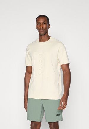 Cremefarvet kortærmet t-shirt med prægede "BOSS" logo, parret med olivengrønne shorts med trykt sort logo på venstre ben.