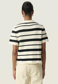 Gestreepte gebreide top met korte mouwen in off-white en zwart. Heeft een ronde kraag en textuurstof, gecombineerd met lichte broek.
