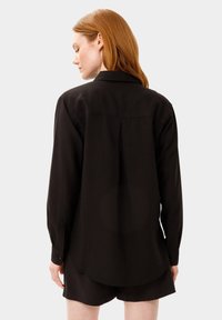 Camicia nera a maniche lunghe con colletto, polsini abbottonati e orlo curvo. Il tessuto appare liscio con una leggera lucentezza.