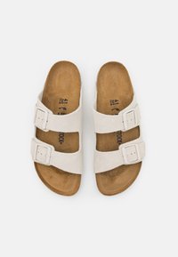 Sandales avec deux boucles réglables, en daim beige clair, avec une semelle intérieure rembourrée marron et une semelle plate. Étiquette de taille visible.