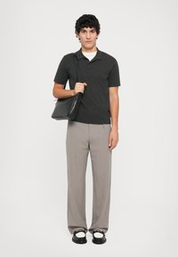 Polo shirt grigio scuro, pantaloni grigi chiari su misura, sandali neri e una borsa a tracolla in pelle nera, caratterizzati da trame morbide e una vestibilità rilassata.