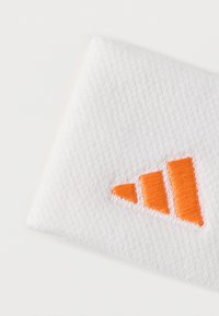 Biely textil s vyšívaným oranžovým trojuholníkovým logom. Textúra je tkaná a okraje sú mierne ošúchané.