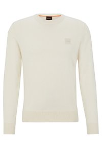 Kraftvit stickad tröja med rund halsringning, ribbade muddar och fåll. Har en subtil logotypmärke på bröstet. Mjuk textur.