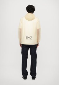 Lightweight, translucent yellow jacket with a hood and gray accents. Features "EA7 Emporio Armani" logo on the back and loose fit design.
