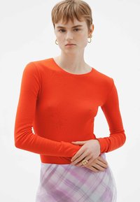 Top ajustado de manga larga rojo con escote redondo. Textura suave, costuras mínimas, combinado con una falda de cuadros en tonos pastel.