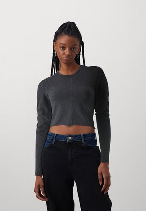 Black cropped long-sleeve top with a textured finish and round neckline. Paired with dark denim pants featuring a contrasting blue waistband.