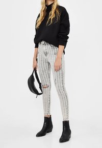 Černý oversized svetr, roztrhané bílé džíny s vertikálními pruhy, černé kotníkov é boty a malá černá crossbody taška.