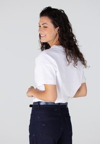 Witte T-shirt met korte mouwen en een relaxte fit, gecombineerd met donkerblauwe denim jeans met subtiele patronen, gedragen met een glanzende zwarte riem.