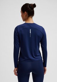 Marineblaues langärmliges Sportoberteil mit rundem Ausschnitt, glatter Textur und einem weißen Logo auf dem oberen Rücken. Verfügt über flache Nähte und eine taillierte Passform.