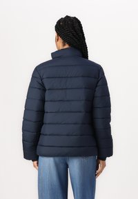 Jachetă puffer aurie, matlasată, de culoare bleumarin, cu guler înalt, panouri verticale și manșete elastice. Țesătură lucioasă cu o finisare curată la tiv.