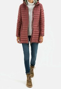 Maroon puffer jacket with vertical stitching, hood, and two side pockets. Worn over a grey knit sweater and blue jeans, paired with brown lace-up boots.