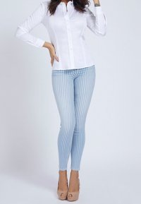 Chemise blanche à manches longues et jean skinny rayé bleu clair, associés à des escarpins à bout ouvert beiges. Tissu lisse et coupe ajustée.
