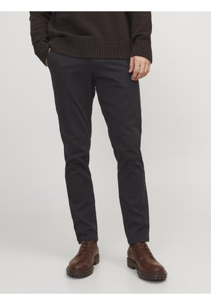 Svarta chinos i lätt tyg, slim-fit design med en mjuk textur. Kombinerat med bruna läderskor och en mörk stickad tröja.