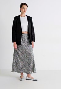 Černý blazer přes bílý crop top, doplněný dlouhou vzorovanou sukní v pastelových barvách. Stříbrné ploché boty dokončují celý vzhled.