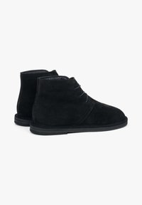 Czarne zamszowe botki za kostkę na niskim obcasie, zaokrąglonym noskiem i wiązaniem na sznurowadła. Miękka faktura i minimalistyczna sylwetka zwiększają uniwersalność.