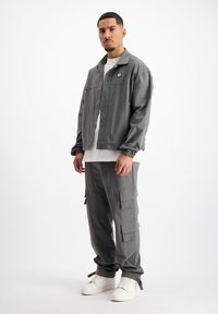 Grijze jas met kraag, borstzak en logo, gecombineerd met bijpassende cargobroek met meerdere zakken en strakke boorden. Witte sneakers.