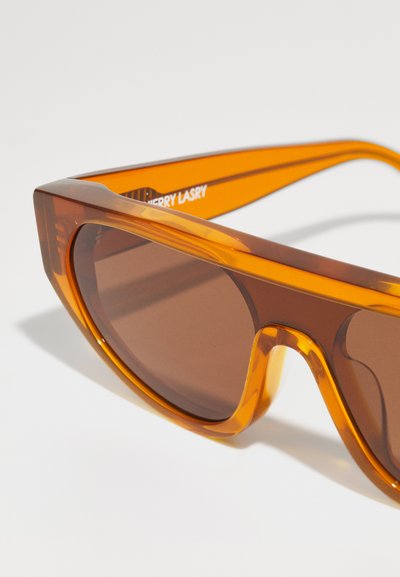 Orange transparent sunglasses with angular frames, brown lenses, and textured temple accents. Brand name "CHERRY LASRY" visible inside.