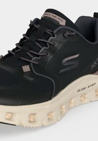Baskets Skechers Glide-Step noires avec semelle beige, lacets gris et col rembourré, avec dessus en mesh et matériaux synthétiques.