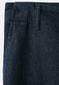 Temno denim blago s tkanjem twill, s ploskim pasom in zankami za pas, prikazuje subtilne kontrastne šive in gladko teksturo.