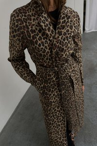 Leopardmønstret trenchcoat i beige og brune nuancer, med bælte i taljen, klapkrave og lange ærmer, fremstillet af tekstureret stof.