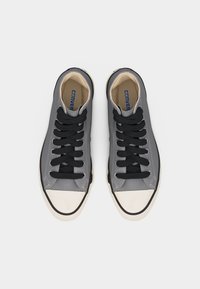 Par grå høye canvas-sneakers med svarte lisser og hvite gummitåhetter sett ovenfra.