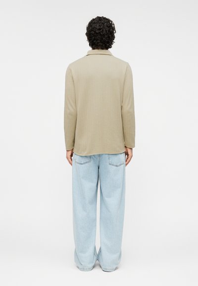 Μπεζ μακρυμάνικο πουκάμισο με γιακά, σε υφασμάτινη υφή. Χαλαρά ανοιχτό μπλε τζιν με πίσω τσέπες και ίσια γραμμή στο πόδι.