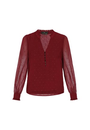 Blouse rouge avec de longues manches transparentes, un col rond, une patte de boutonnage sur le devant et un motif texturé subtil. Présente des poignet et un ourlet à volants.
