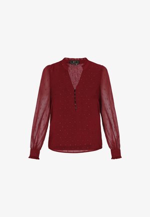 Punane pluus pikkade läbipaistvate varrukatega, ümmarguse kaelusega, ees nööpidega ja peene tekstuuriga mustriga. Omab volangiga mansette ja äärt.