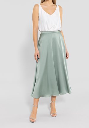 Jasnozielona satynowa spódnica o luźnym kroju typu A, zestawiona z białym, bezrękawnym topem. Strój ma dekolt w szpic i delikatny połysk.