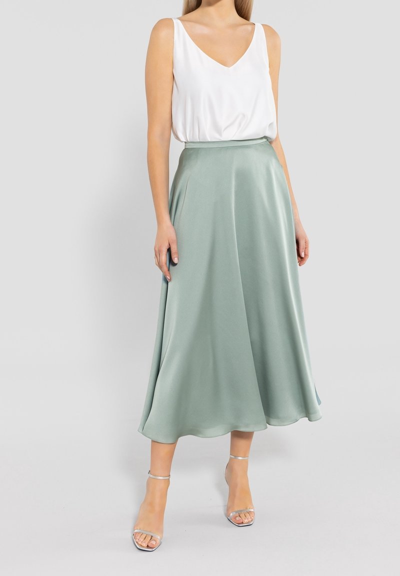 Jupe en satin vert clair avec une silhouette fluide en ligne A, associée à un haut blanc sans manches. La tenue présente un décolleté en V et un éclat doux.