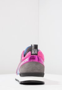 Šedé, růžové a modré tenisky s textem "LOVE MOSCHINO" na poutku na patě a lesklým růžovým páskem nad patou, z pohledu zezadu.